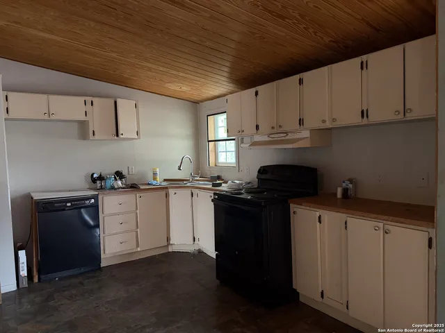 a kitchen with granite countertop a sink dishwasher a stove and white cabinets