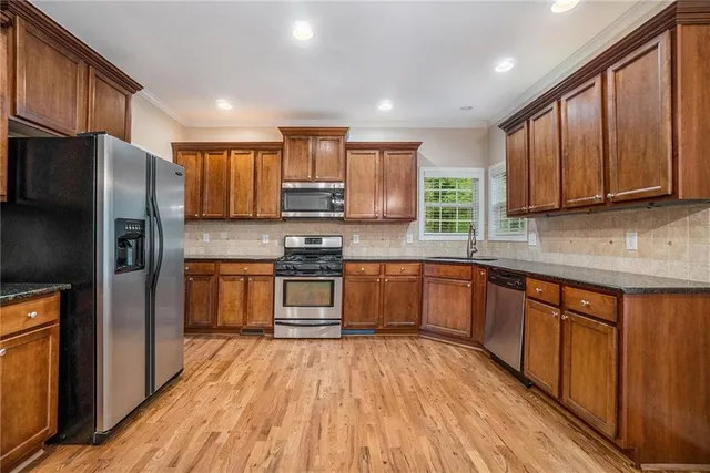 a kitchen with stainless steel appliances wooden floors cabinets and a window