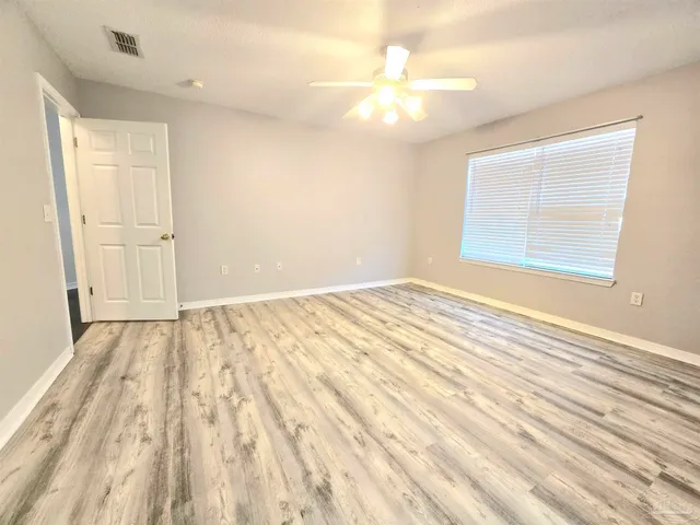 an empty room with wooden floor fan and windows