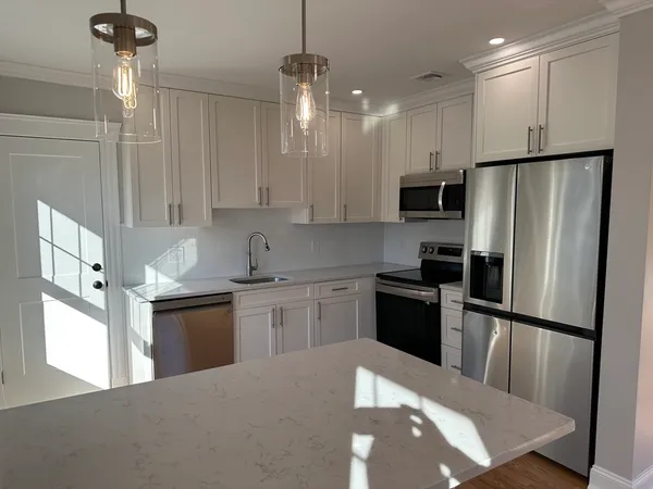 a kitchen with stainless steel appliances granite countertop a refrigerator a sink dishwasher a stove and white cabinets with wooden floor