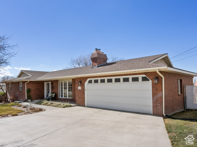 Ranch-style home featuring brick siding, a chimney, an attached garage, fence, and a front yard