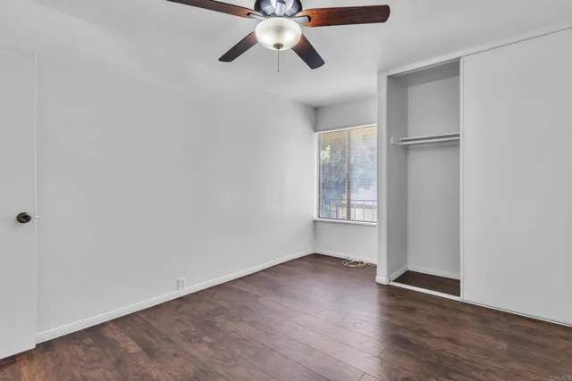 an empty room with wooden floor chandelier fan and windows