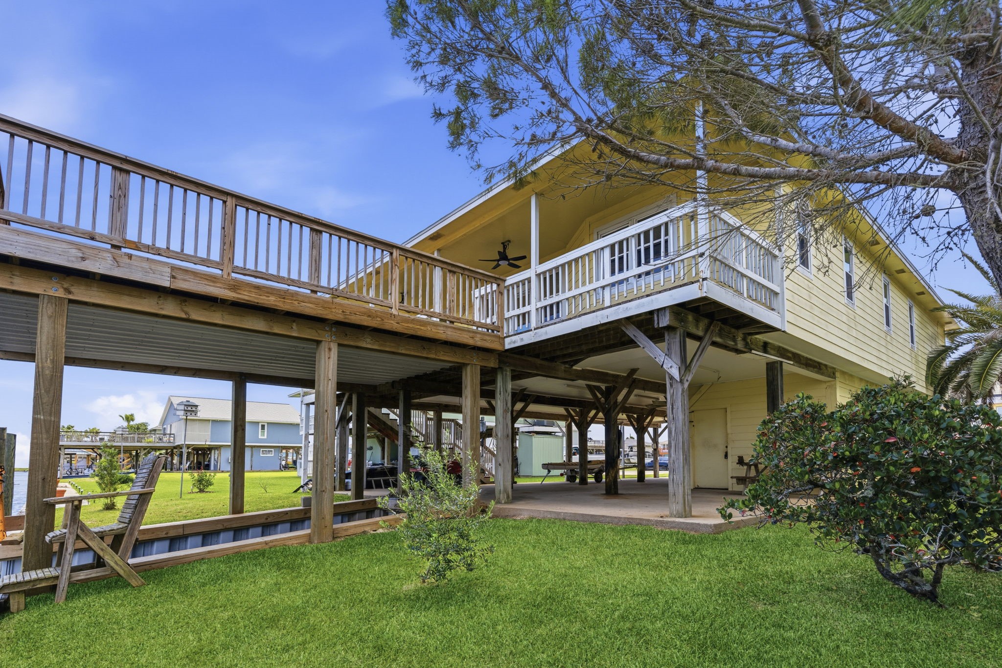 119 Sand Shoals Road Freeport, TX 77541 - Photo 15 of 34 Rear elevation — elevated coastal home on pilings with full-length covered porch, ground-level shaded pad for parking and gear storage, and bulkhead canal frontage.
