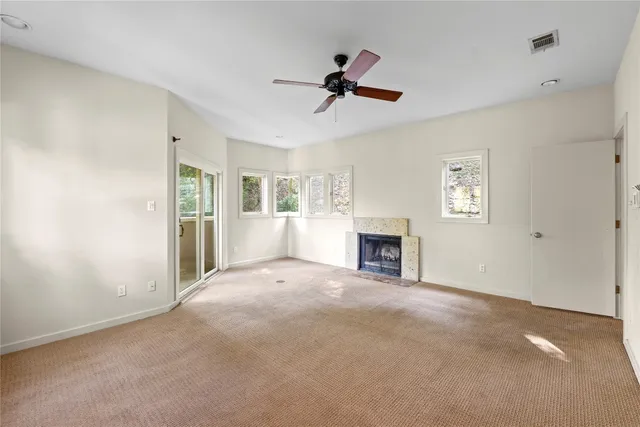 a view of a livingroom with a fireplace a ceiling fan and windows