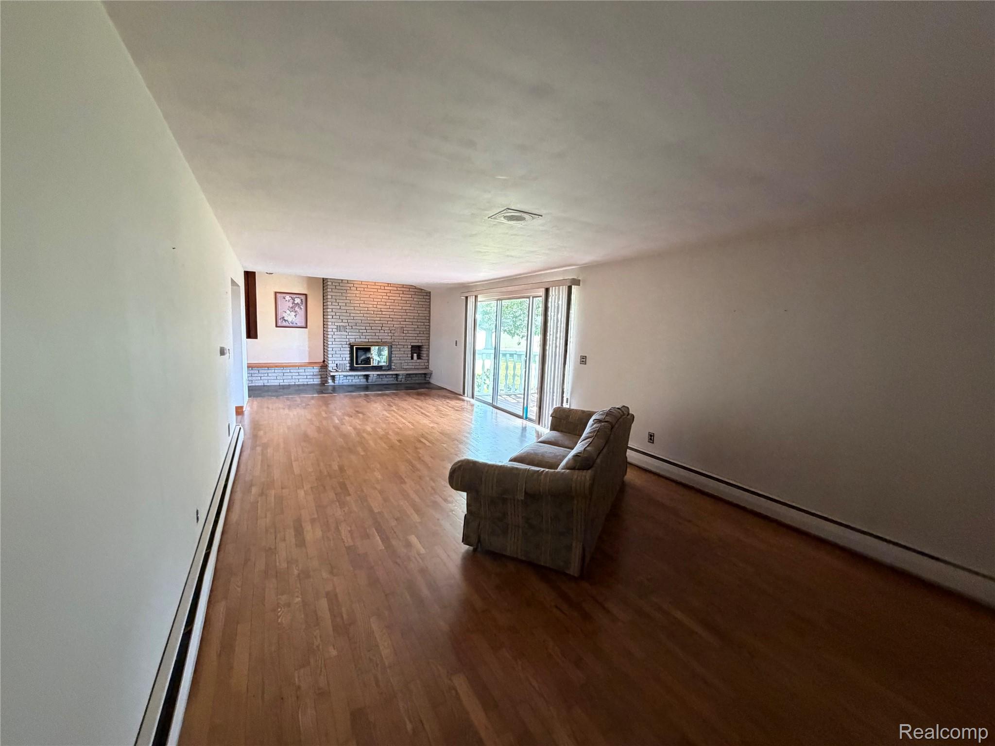 8886 East Burnside Road Brown City, MI 48416 - Photo 13 of 22 Spacious interior featuring wood-finish flooring, a full-height stone fireplace with hearth, and sliding glass doors
