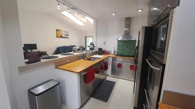 a living room with stainless steel appliances furniture a rug kitchen view and a large window