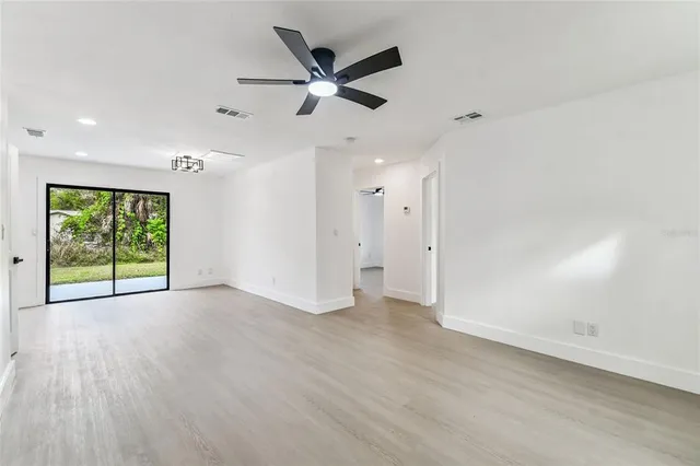 an empty room with wooden floor fan and windows