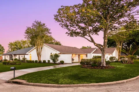 a view of a white house next to a yard with big trees