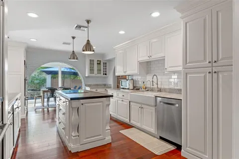 a kitchen with stainless steel appliances kitchen island granite countertop a stove a sink a refrigerator and white cabinets with wooden floor