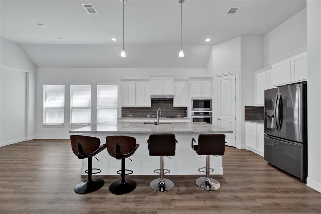 2307 Sam Street Mansfield, TX 76063 - Photo 14 of 23 Kitchen featuring stainless steel appliances, white cabinets, a kitchen island with sink, light stone counters, and lofted ceiling