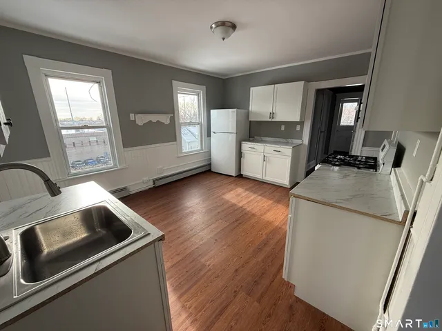 a kitchen with stainless steel appliances granite countertop a refrigerator a stove a sink dishwasher and white cabinets with wooden floor