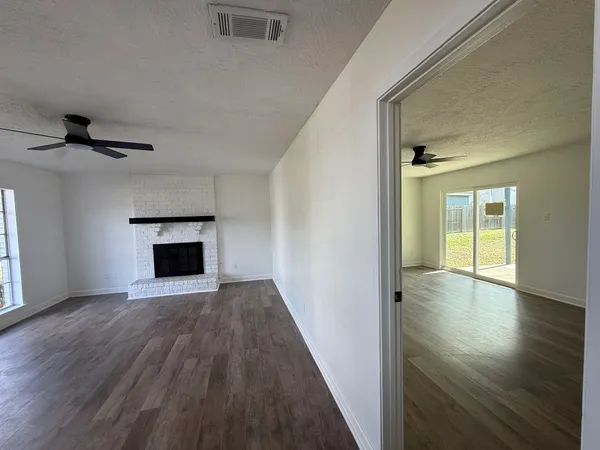 a view of an empty room with wooden floor fireplace and a window