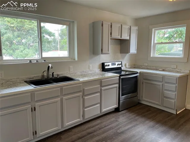 a kitchen with stainless steel appliances white cabinets a sink a window and wooden floors