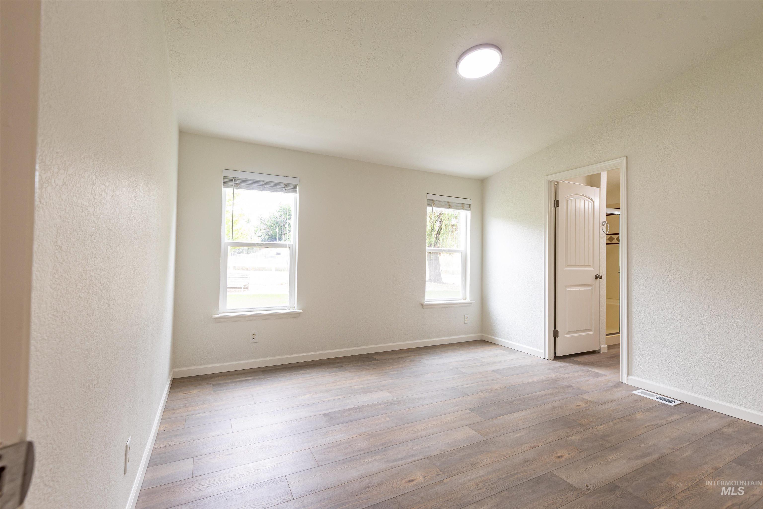17028 Lower Pleasant Ridge Road Caldwell, ID 83607 - Photo 8 of 21 Spacious room featuring wood-finish flooring, two large windows with white trim, a semi-flush mount ceiling light, and an interior door with a paneled design