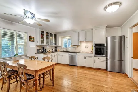 a kitchen with a refrigerator a stove a sink dishwasher a dining table and chairs with wooden floor