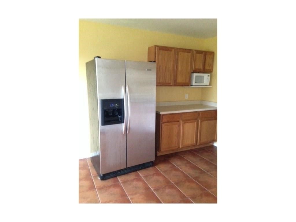 120 Rinehardt Street Hutto, TX 78634 - Photo 2 of 7 Kitchen with stainless steel fridge with ice dispenser, brown cabinetry, light countertops, white microwave, and dark tile patterned floors