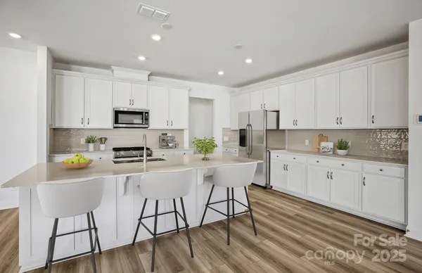a kitchen with stainless steel appliances a stove a sink a refrigerator white cabinets and wooden floor