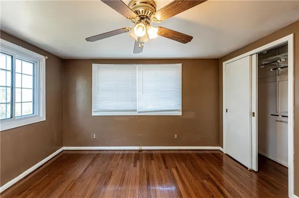an empty room with wooden floor chandelier fan and windows