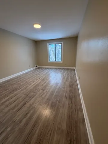a view of an empty room with wooden floor and window
