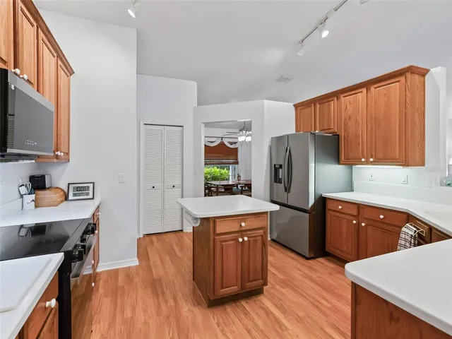 a kitchen with stainless steel appliances granite countertop a kitchen island a stove a sink a refrigerator white cabinets and wooden floor