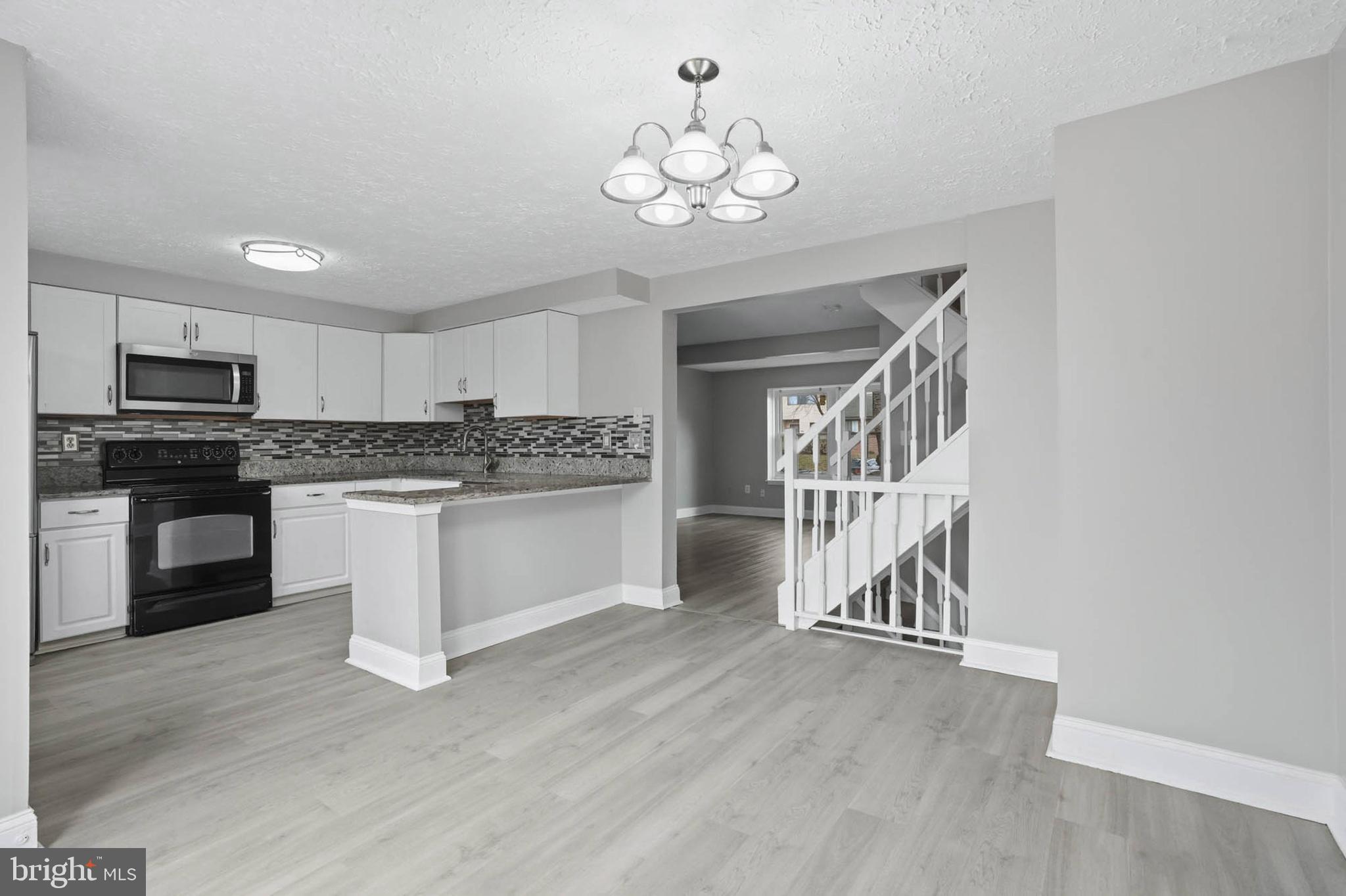 9931 Tuscarora Road Randallstown, MD 21133 - Photo 4 of 30 a white kitchen with wooden floor and stainless steel appliances