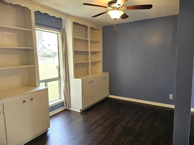 an empty room with wooden floor cabinet and windows