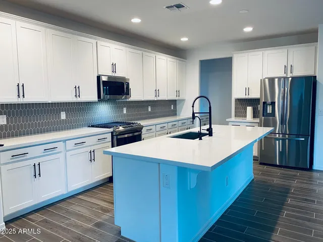 a kitchen with stainless steel appliances granite countertop a stove top oven a sink and white cabinets with wooden floor