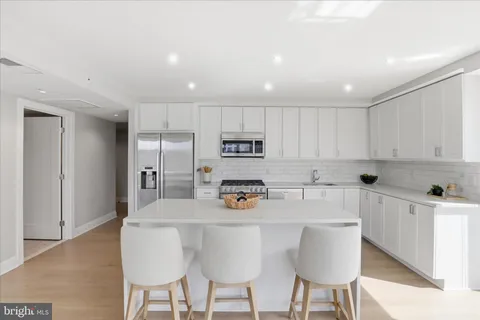 a kitchen with stainless steel appliances kitchen island granite countertop a sink a stove a refrigerator with white cabinets a table and chairs