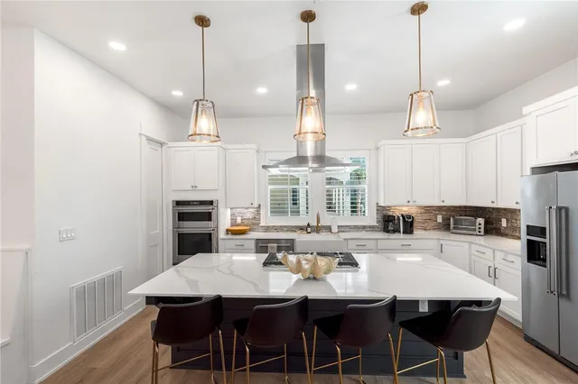 a kitchen with stainless steel appliances kitchen island granite countertop a dining table chairs and a refrigerator