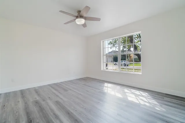 an empty room with wooden floor fan and windows