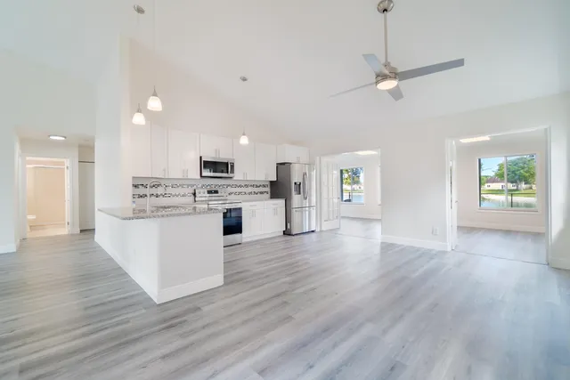 a view of an empty room and kitchen with wooden floor