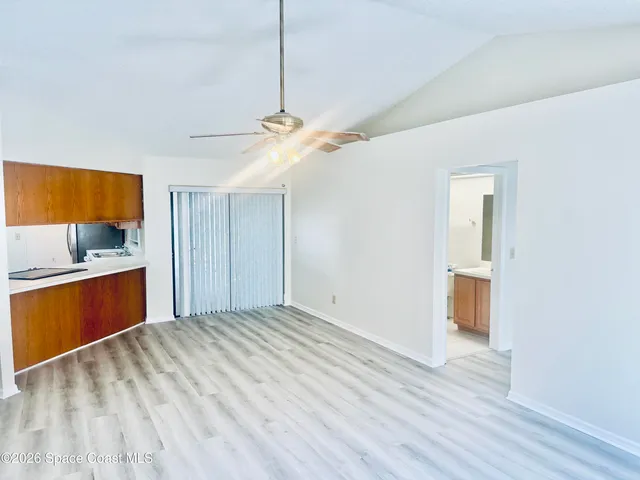 a view of empty room with wooden floor and kitchen view