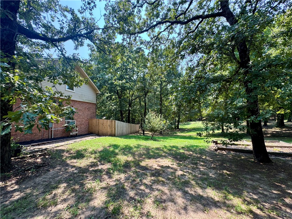 1197 Ridgeview Lane Russellville, AR 72802 - Photo 42 of 44 Expansive outdoor space featuring a partial brick and siding exterior, a new wood privacy fence, mature trees, and a landscaped bed with dark mulch