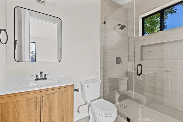 a bathroom with a toilet a sink a glass door a shower a mirror and vanity