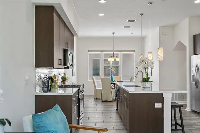 a kitchen with stainless steel appliances granite countertop a refrigerator a sink a stove and a dining table with wooden floor