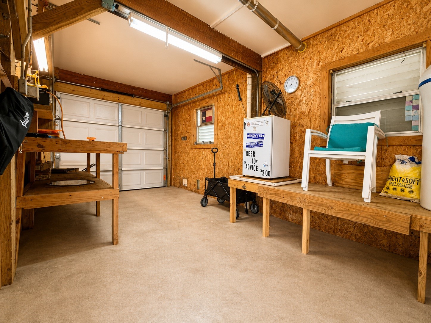 135 Sand Shoals Road Freeport, TX 77541 - Photo 19 of 20 This photo shows a spacious, well-lit garage with a workbench and ample storage space. It features a finished interior with wood paneling, a small fridge, and a window for natural light. Perfect for DIY projects or additional storage.