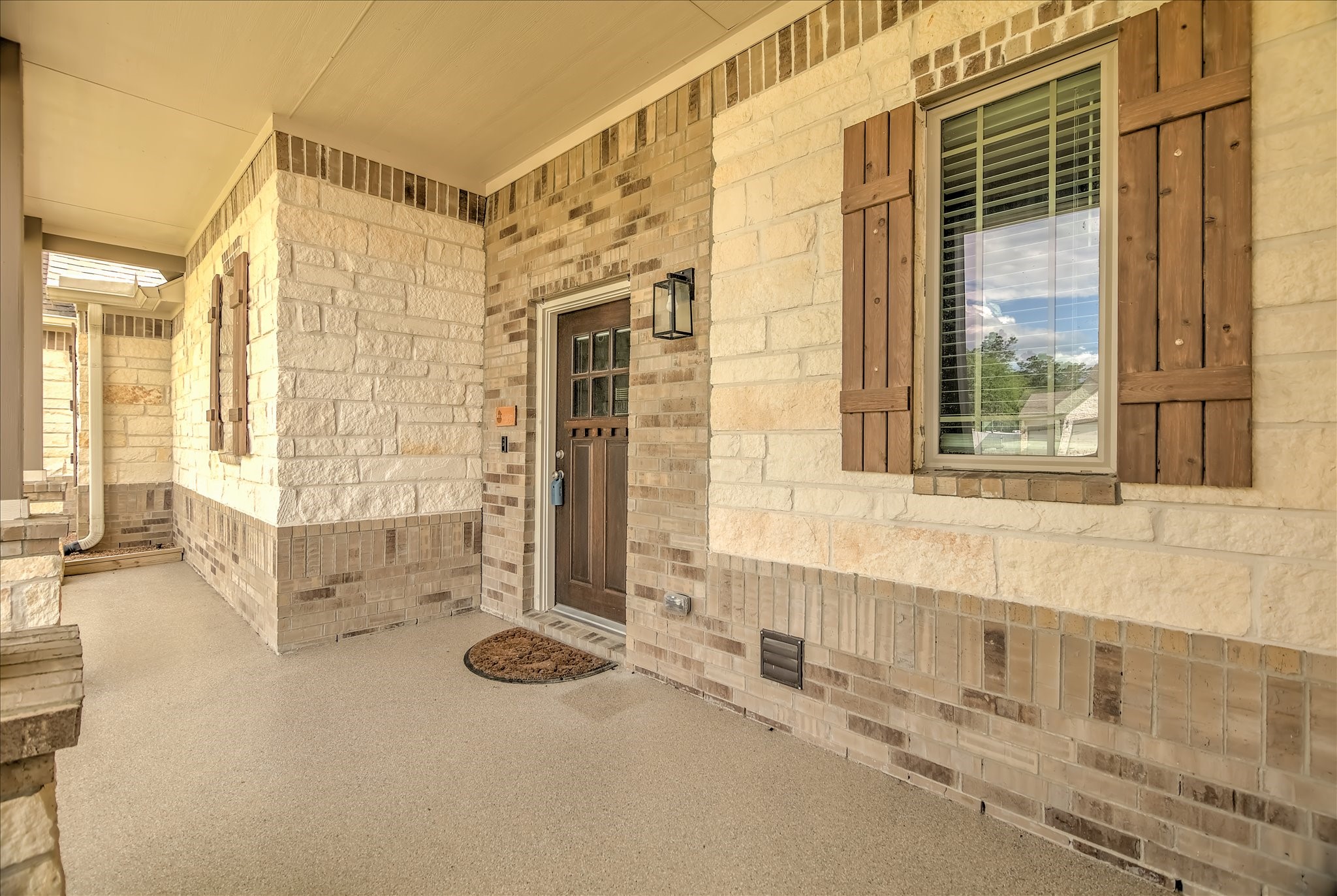 16738 Rockwall Street Conroe, TX 77303 - Photo 3 of 42 Covered front entry featuring a solid wood door, decorative shutters, and classic stone and brick accents. The sheltered porch provides a warm, inviting arrival for guests and everyday convenience.