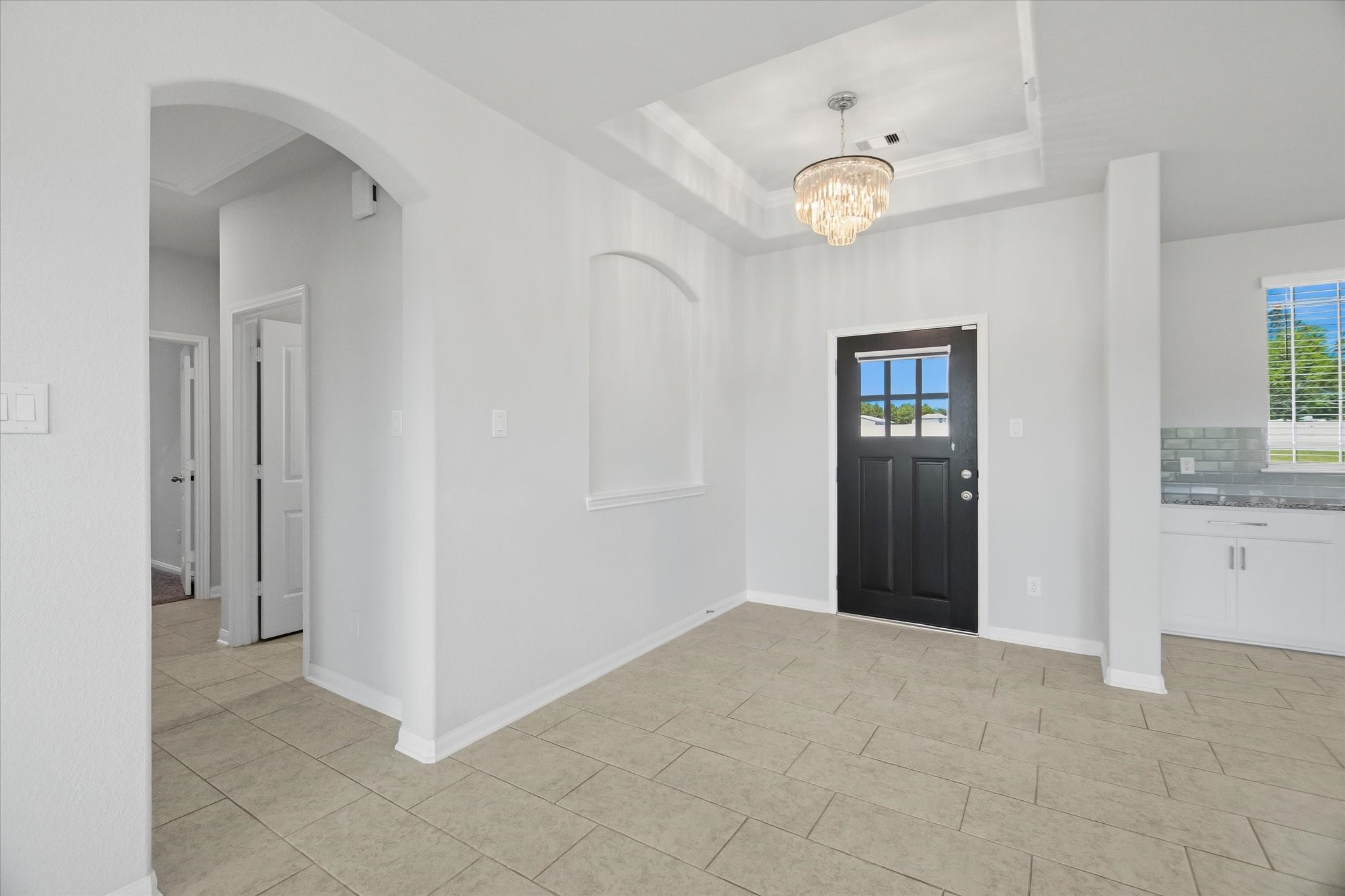 16738 Rockwall Street Conroe, TX 77303 - Photo 5 of 42 Stepping through the front door, you’re greeted by an inviting entry. A tray ceiling draws the eye upward, while a custom chandelier casts a warm, elegant glow across the space. An arched art niche adds architectural character, perfect for showcasing a favorite piece or seasonal décor.