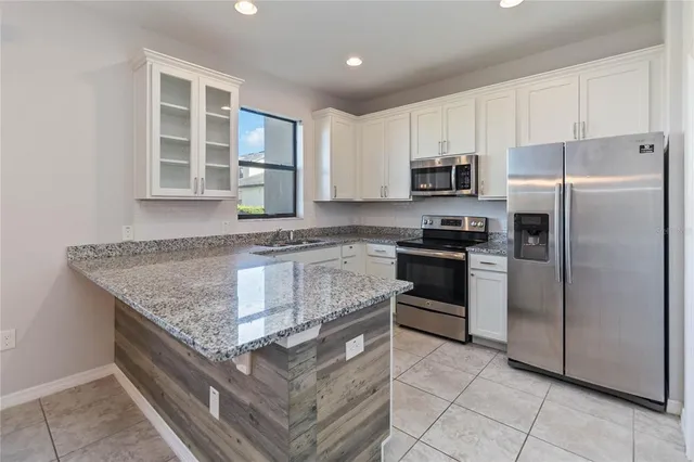 a kitchen with granite countertop a refrigerator a stove a sink and white cabinets with wooden floor