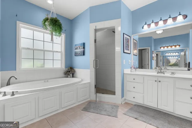 a spacious en suite bathroom with a double vanity sink a large mirror and a bathtub next to a window