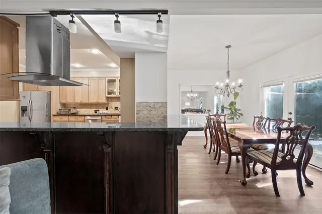 a dining hall with stainless steel appliances kitchen island granite countertop a table chairs and a wooden floor