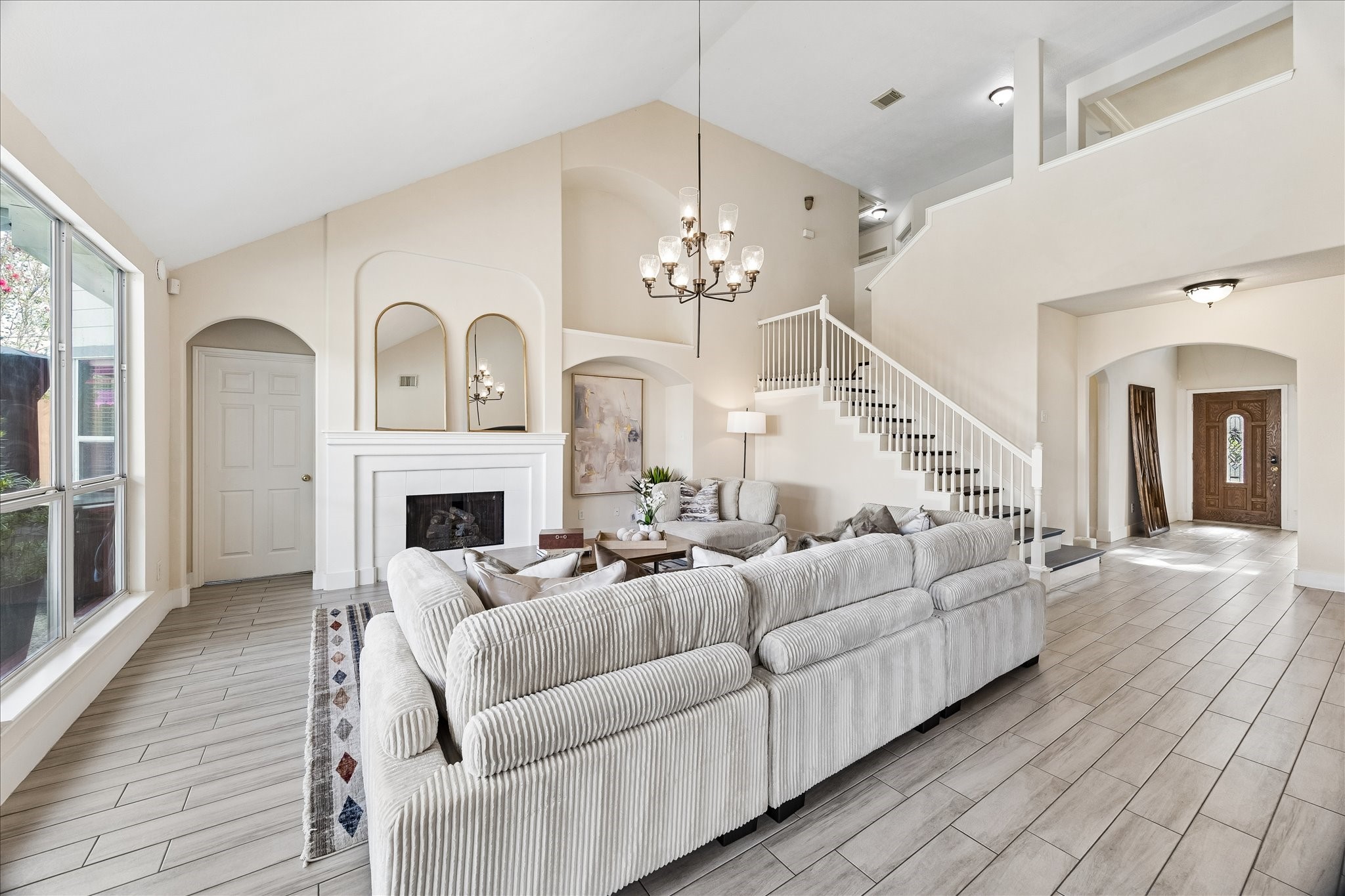 20923 Wind Field Lane Spring, TX 77379 - Photo 10 of 29 Spacious living room with high ceilings, featuring a cozy fireplace, elegant chandelier, and abundant natural light from large windows. The open staircase adds a touch of sophistication, leading to the upper level.