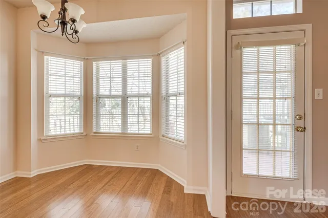 an empty room with wooden floor chandelier and windows