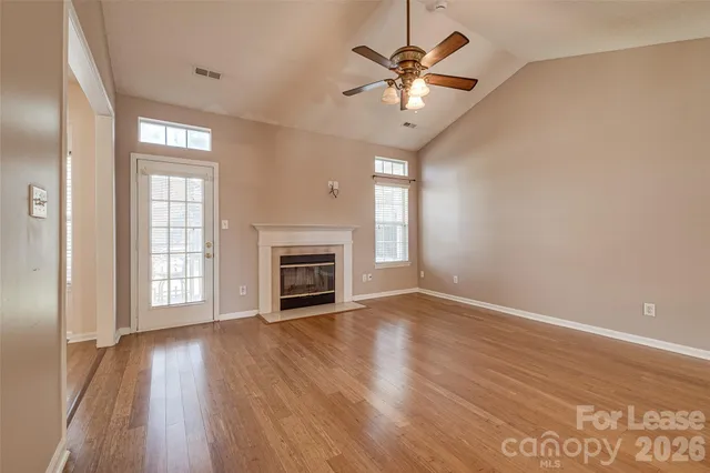 an empty room with wooden floor fireplace and windows