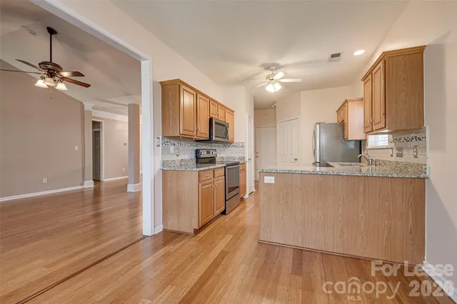 a kitchen with kitchen island granite countertop a stove a sink a refrigerator and white cabinets with wooden floor