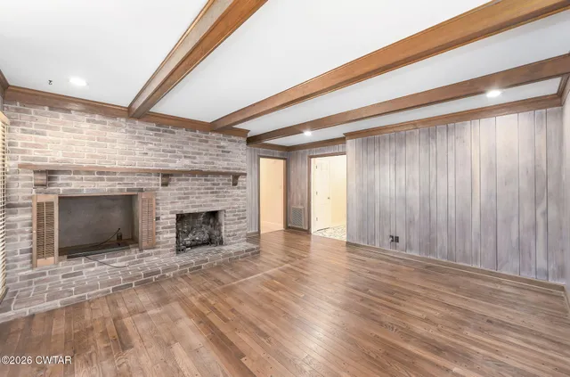 an empty room with wooden floor fireplace and windows