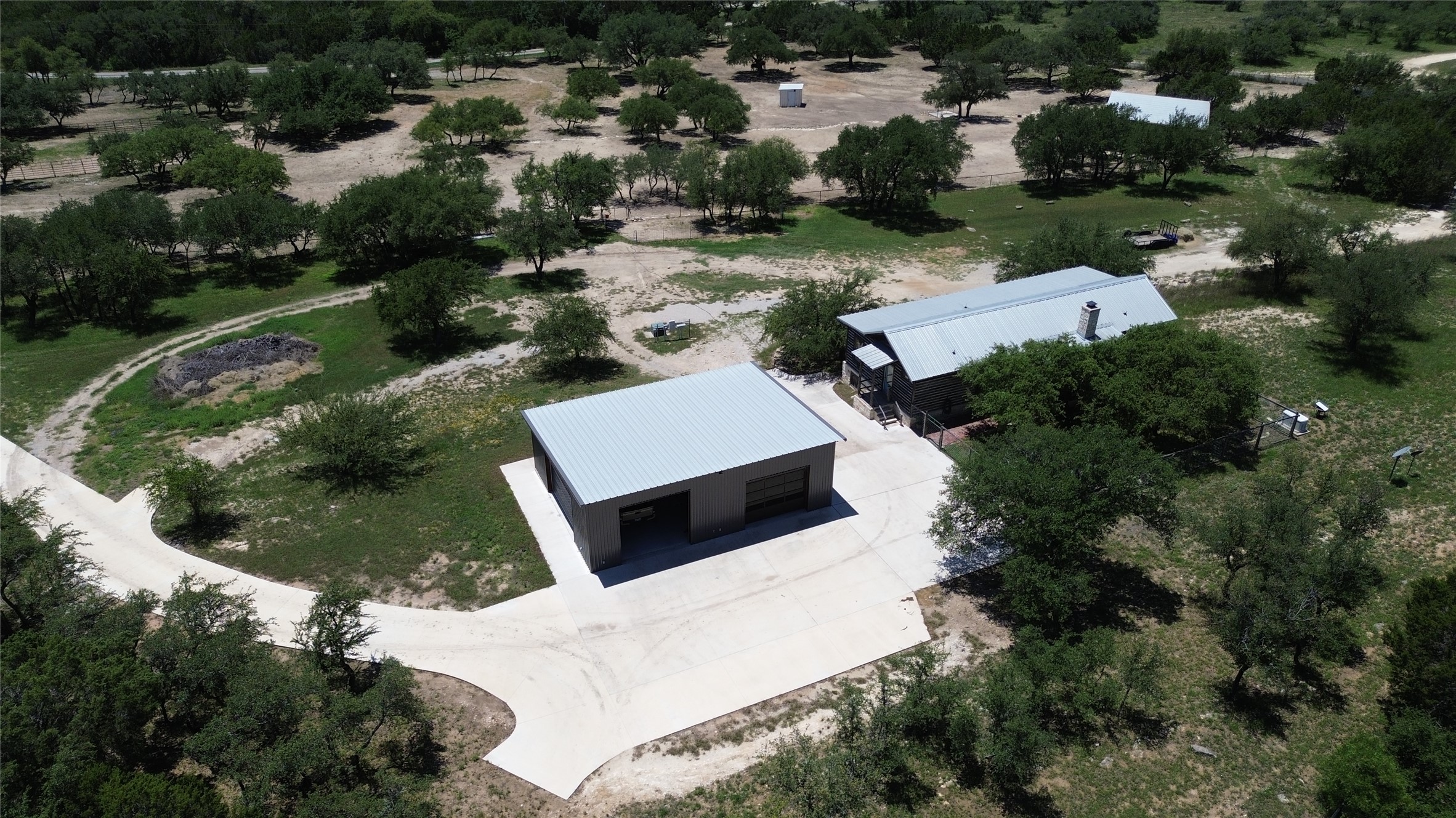 496 Middleton Road Spicewood, TX 78669 - Photo 38 of 40 An aerial perspective reveals a secluded retreat featuring a main structure and a detached garage, nestled among mature trees.