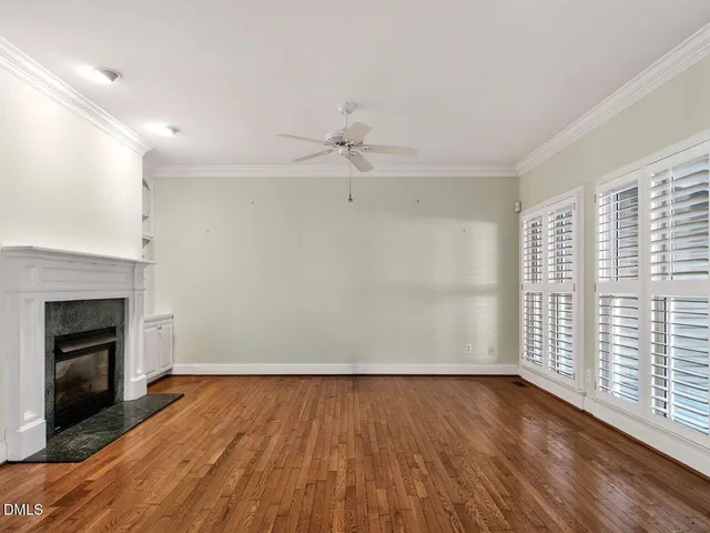 an empty room with wooden floor fireplace and windows