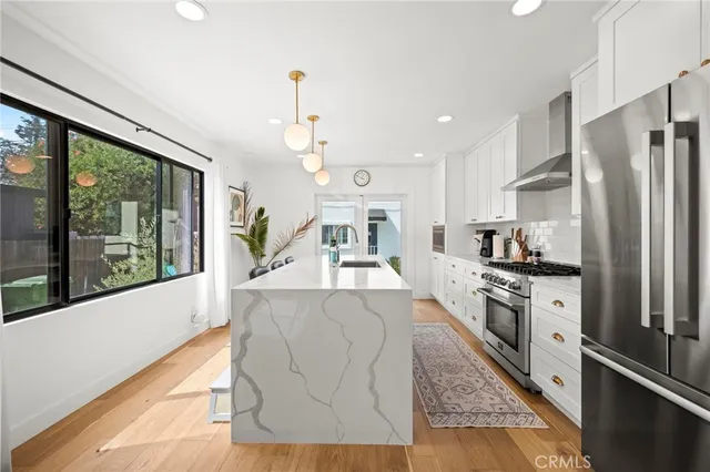 a large kitchen with stainless steel appliances granite countertop a refrigerator a oven a stove and a dining table with wooden floor