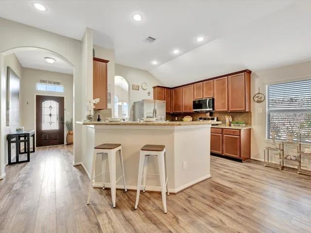 a kitchen with stainless steel appliances a stove a sink dishwasher a refrigerator white cabinets and wooden floor next to a window